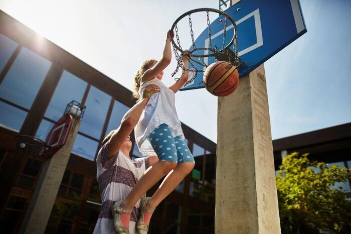 Ein Mädchen spiele Basketball. Ein Mann hebt sie hoch an den Korb. Der Ball fliegt durch den Korb, Foto: David Maurer, Lebenshilfe