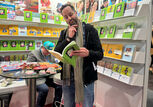Ein Mann liest ein Buch auf einer Buchmesse. Er steht an einem Stand mit vielen bunten Büchern.