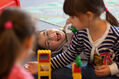 Blick durch zwei spielende Mädchen auf am Boden liegenden, lachenden Jungen (Foto: Sybille Baier)