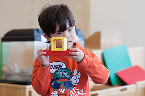 Kind mit Down-Syndrom blickt durch eine aus Duplosteinen gebaute Kamera (Foto: Sybille Baier)