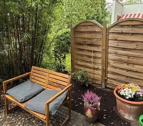 Bild vom Garten der WG 11 der Lebenshilfe Berlin mit Holzmöbeln und geschnittenen Plfanzen.